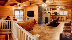 Interior de una cabaña de troncos con chimenea, muebles de madera, televisor y comedor.