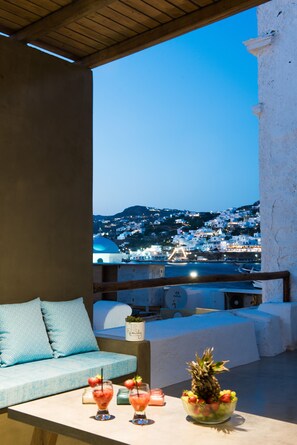 Ein Balkon mit Blick auf eine Hügelstadt, eine Couch mit Kissen sowie ein Tisch mit Getränken und einer Obstschale.