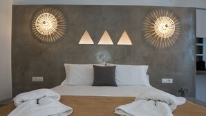 Una habitación de hotel con una cama grande, un cabecero con tres lámparas triangulares y dos toallas sobre la cama.