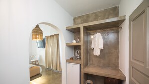 Habitación de hotel compacta con kitchenette, un refrigerador pequeño, zona de estar con una silla y una lámpara colgante.