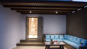 Un área de estar moderna al aire libre con un sofá y una mesa de centro, una escalera que conduce a un espacio interior y una estructura de techo de madera.