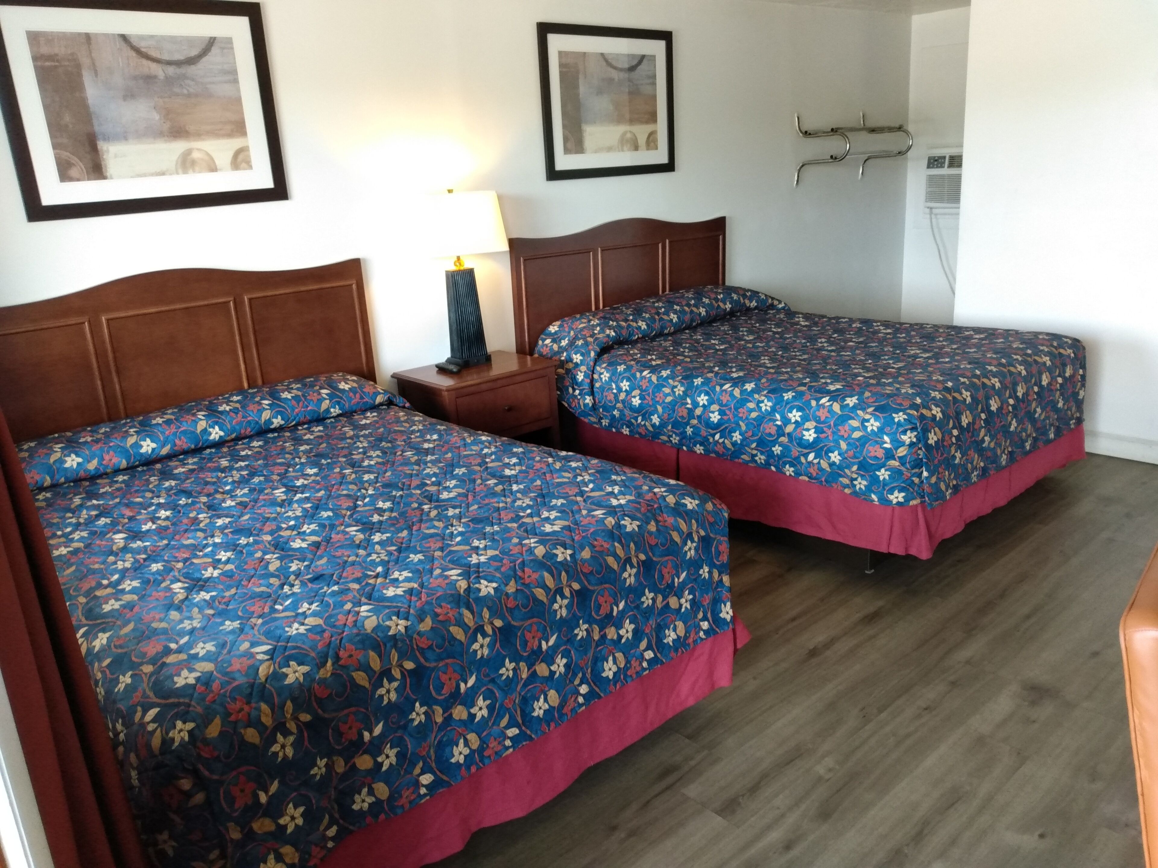 Una habitación con dos camas, una mesita de noche, una lámpara y cuadros en las paredes.