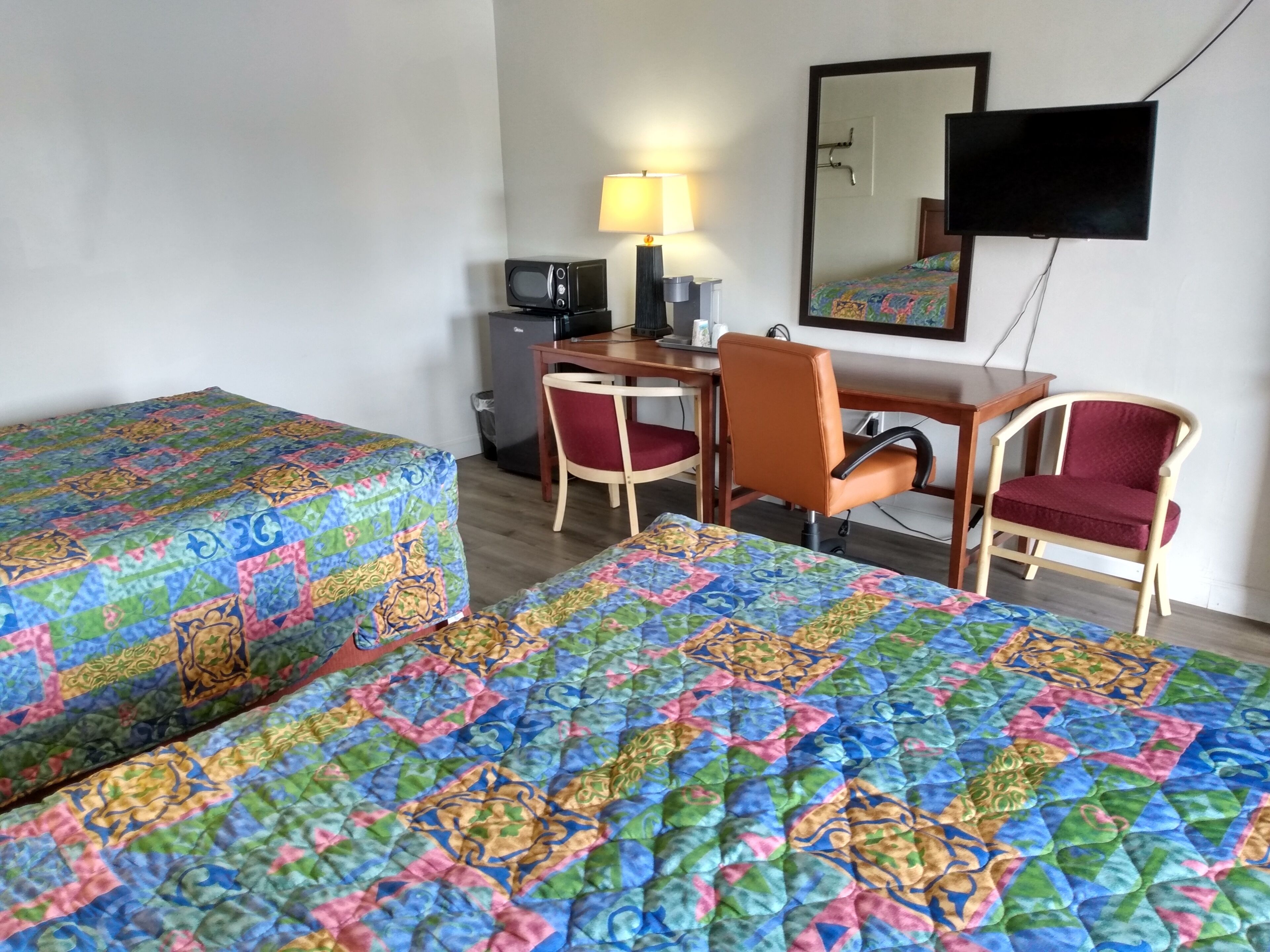 A hotel room with two beds, a desk, a chair, a television, and a refrigerator.