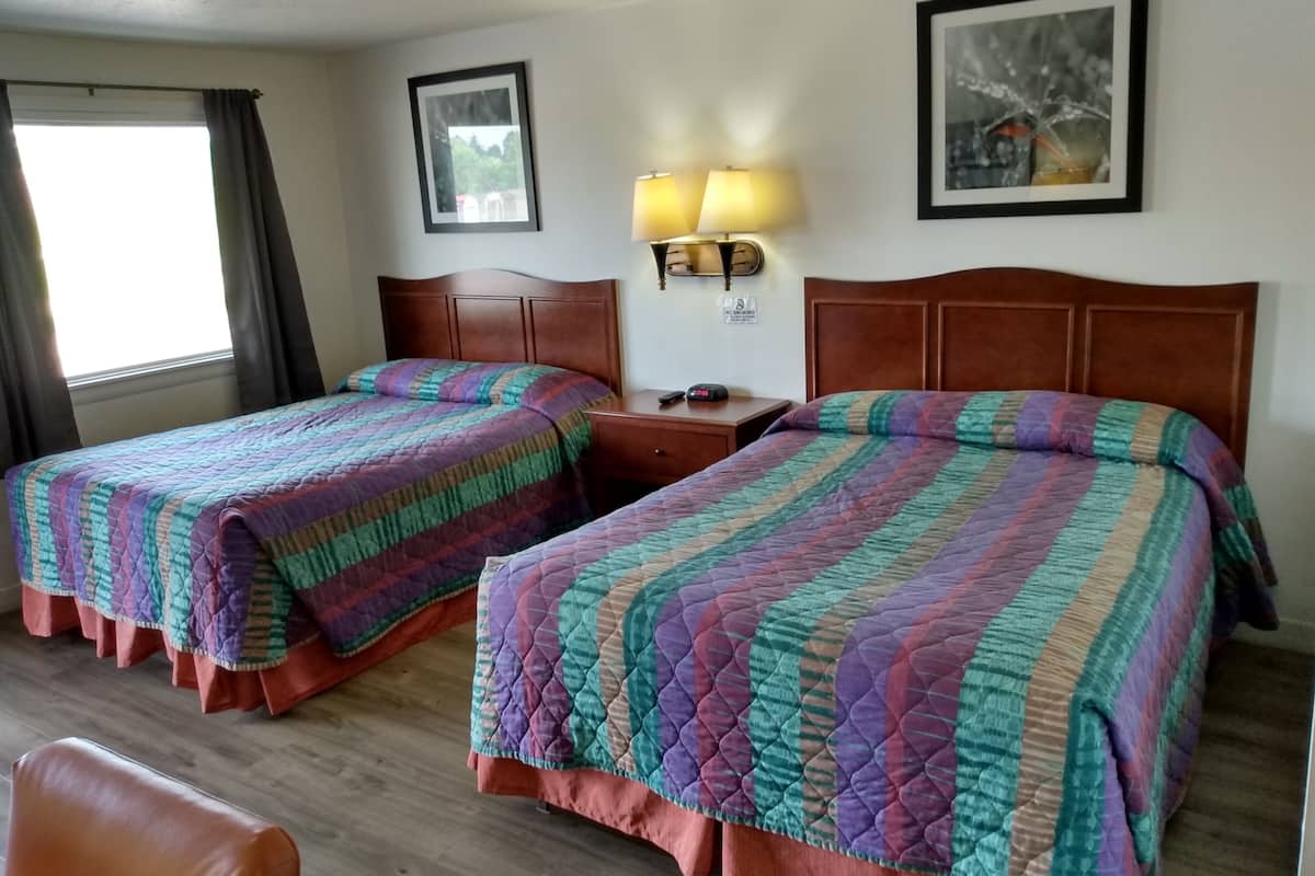 A hotel room with two beds, a nightstand with a lamp, a framed picture on the wall, and a window with curtains.