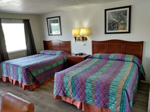 A hotel room with two beds, a nightstand with a lamp, a framed picture on the wall, and a window with curtains. - ELDORADO MOTEL (New Castle)