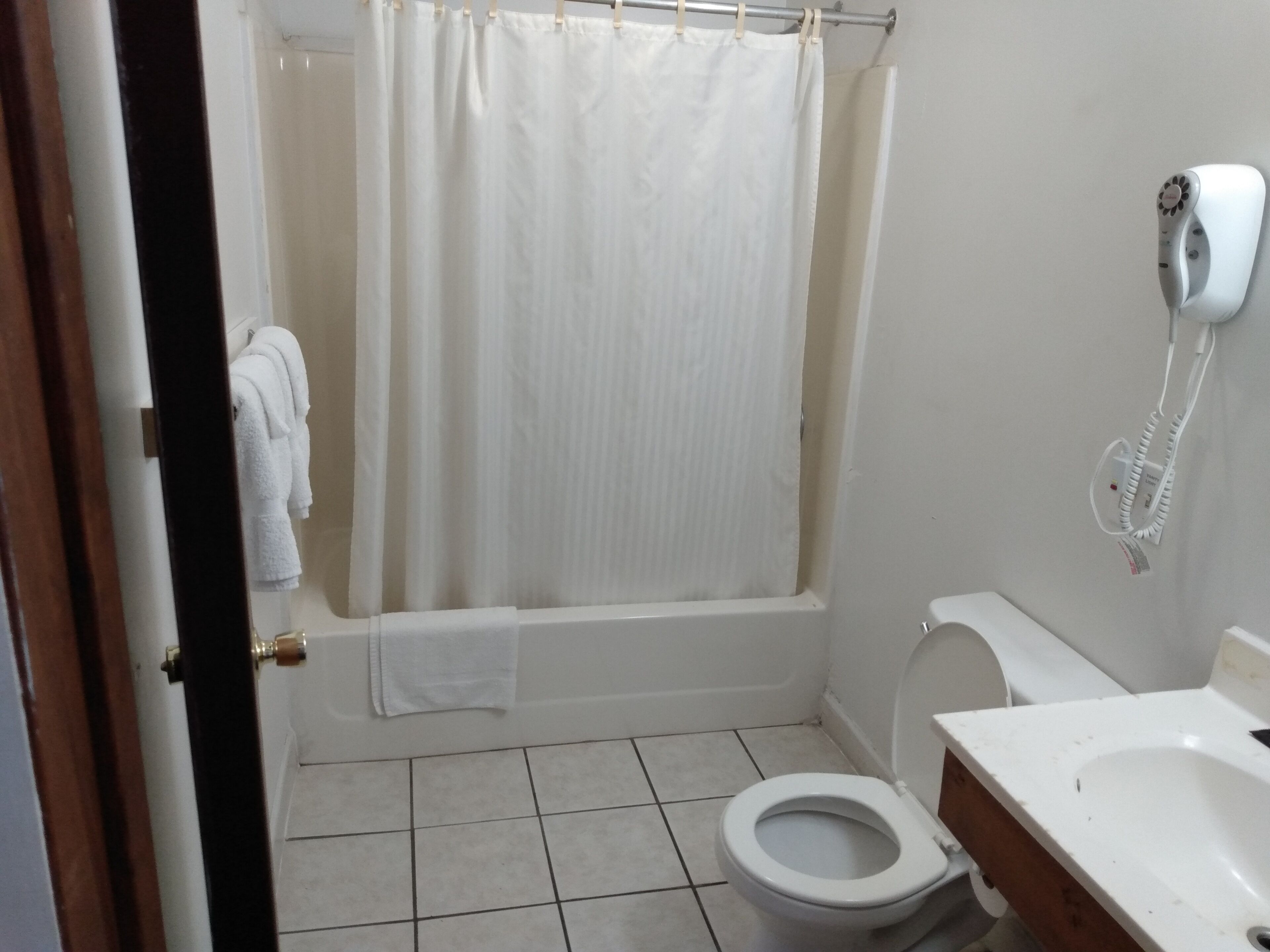 A bathroom with a white toilet, a bathtub with a shower curtain, and a hairdryer mounted on the wall.
