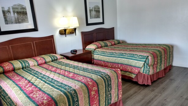 Ett hotellrum med två sängar, var och en med ett randigt sängöverkast, ett trägaveltavla, ett nattduksbord med en lampa och inramade tavlor på väggen.