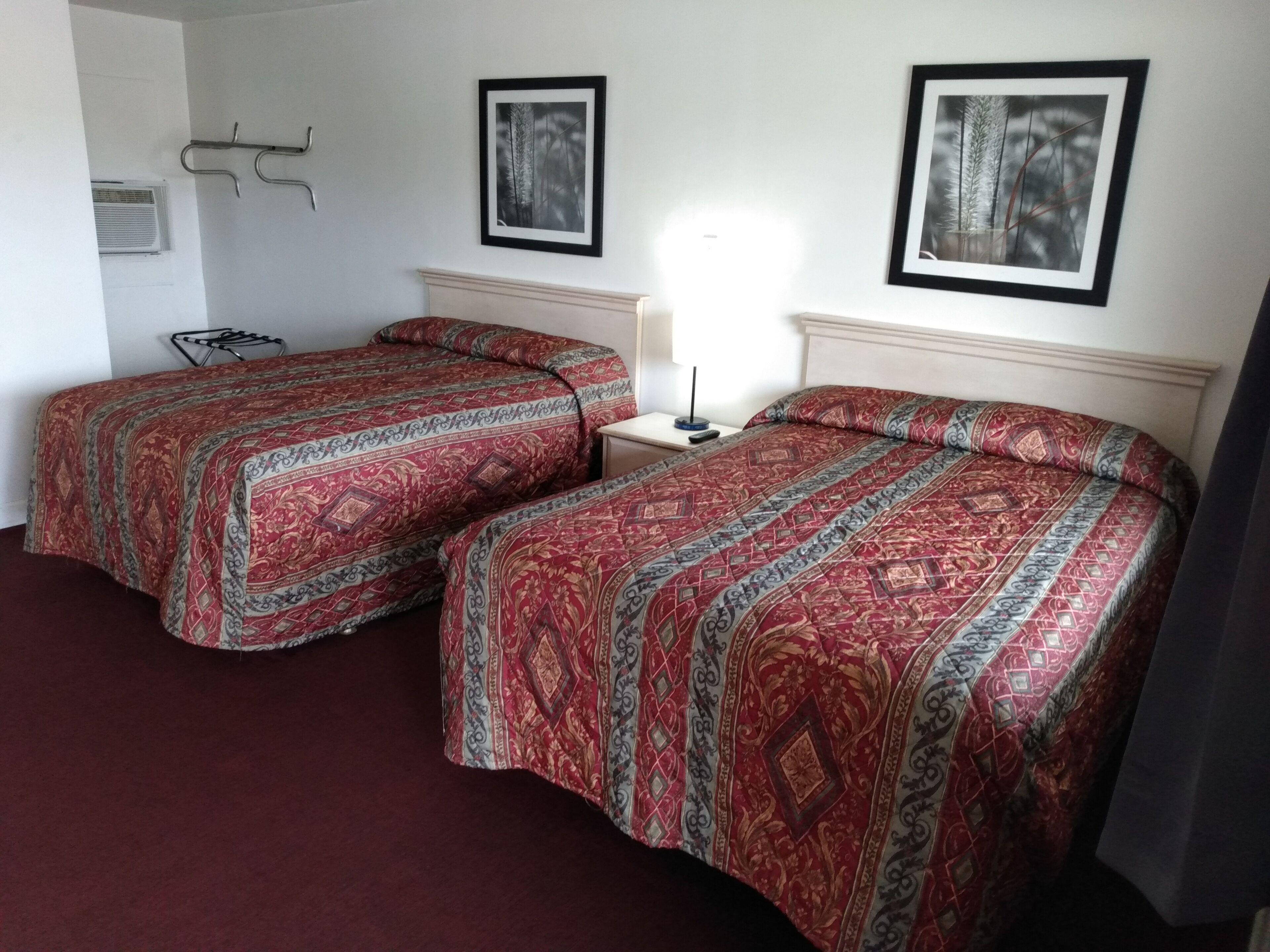 Een hotelkamer met twee bedden, een nachtkastje, een lamp en twee ingelijste foto's aan de muur.
