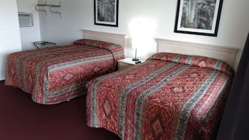 A hotel room with two beds, a bedside table, a lamp, and two framed pictures on the wall.