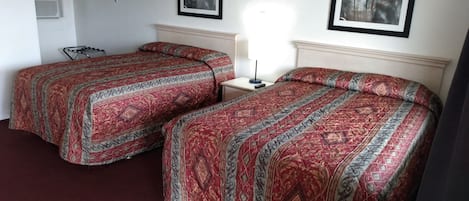 Une chambre d’hôtel avec deux lits, une table de chevet, une lampe et deux tableaux encadrés au mur.