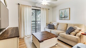 A living room with a wooden coffee table, beige sofa, and a painting of sailboats. - Walk to Beach: Family Hilton Head Island Condo (Hilton Head Island)