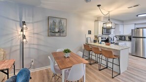 A modern kitchen with white cabinets, stainless steel appliances, and a wooden dining table with white chairs. - Walk to Beach: Family Hilton Head Island Condo (Hilton Head Island)