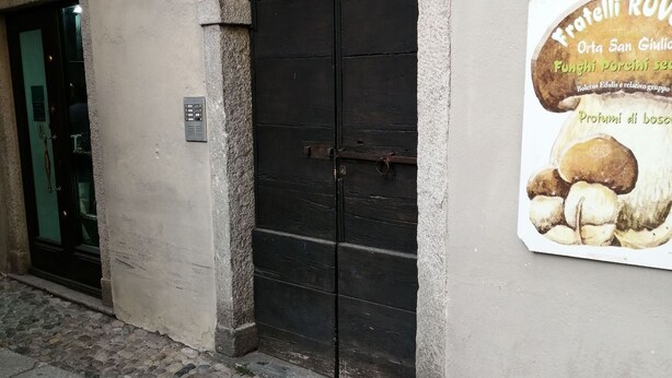 A building with a black door, a stone-paved entrance, and a sign advertising mushrooms. - Beautiful apartment for 4 guests with WIFI, TV and pets allowed (Orta San Giulio)