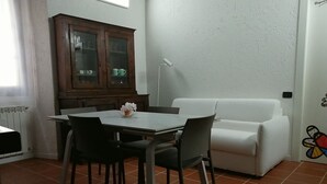 A dining area with a table and chairs, a white sofa, a cabinet with glass doors, and a radiator. - Beautiful apartment for 4 guests with WIFI, TV and pets allowed (Orta San Giulio)