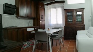 A compact kitchen with wooden cabinets, a dining table with chairs, a white sofa, and a cabinet with glass doors. - Beautiful apartment for 4 guests with WIFI, TV and pets allowed (Orta San Giulio)