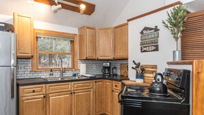 Una cocina con armarios de madera, una estufa negra, un lavamanos y una ventana con vista a árboles.