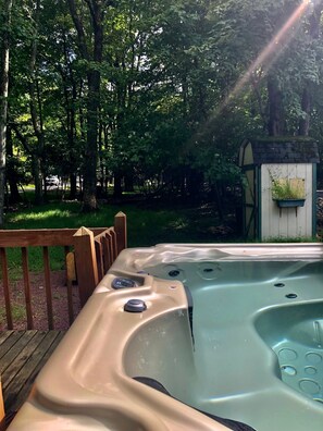 Un jacuzzi con terraza de madera y un cobertizo pequeño en zona boscosa.