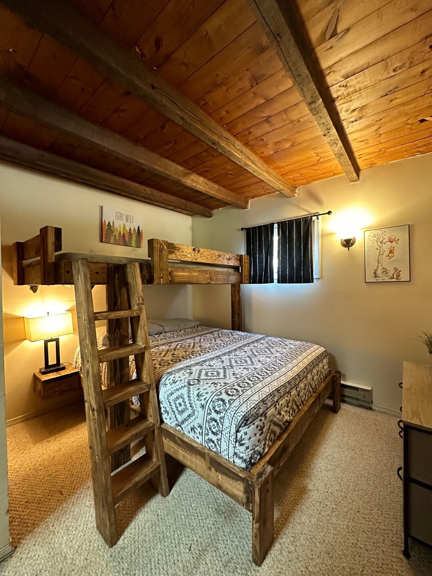 Un dormitorio rústico con literas de madera, una escalera, una mesita de noche con lámpara y un aplique de pared.