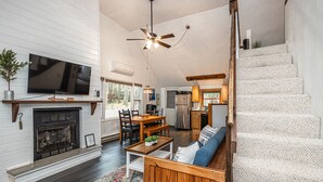 Un salón amplio con chimenea, una mesa de comedor y un sofá. Se observa una cocina al fondo, con un refrigerador y una estufa.