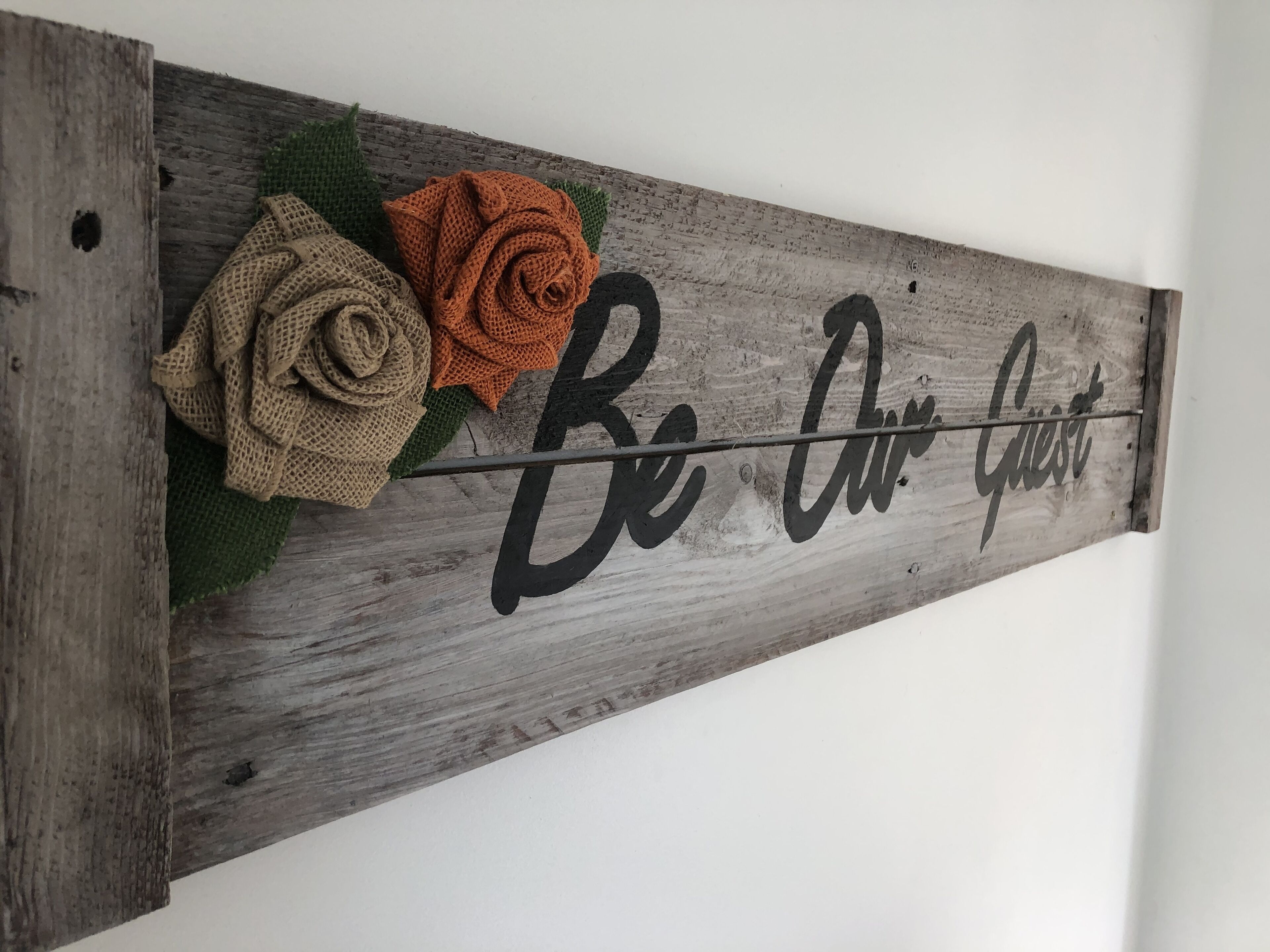 A wooden sign with the words "Be Airy Guest" and decorative flowers.