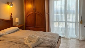 Un dormitorio con cama, armario de madera y ventana con cortinas traslúcidas.