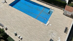 Piscina en la azotea con dos zonas separadas, rodeada de sillas de descanso y sombrillas.