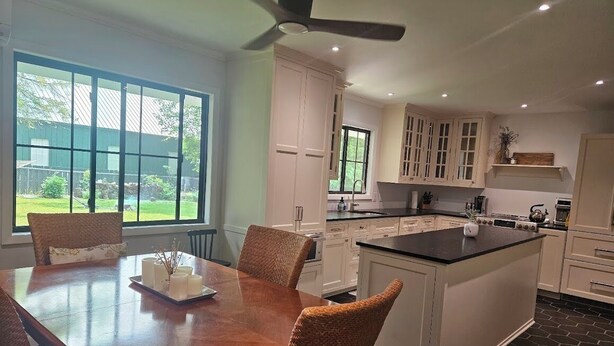 Una cocina amplia con una isla grande, muebles blancos y un comedor con sillas de mimbre.