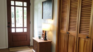 Una puerta de madera con un ventanal, una pequeña mesa de madera con una lámpara y un letrero en la pared.