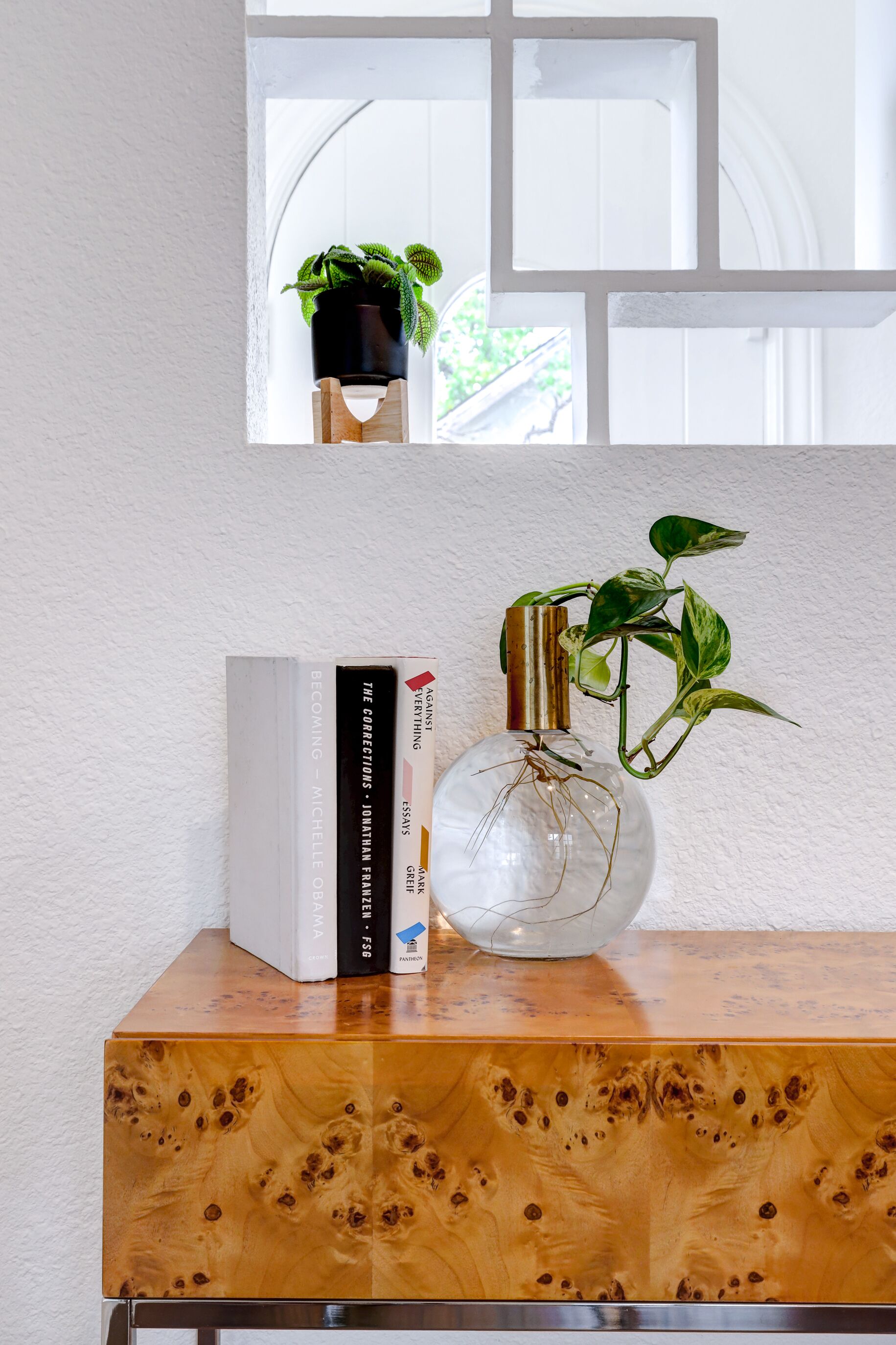 Un meuble en bois contenant un vase en verre avec une plante et des livres.