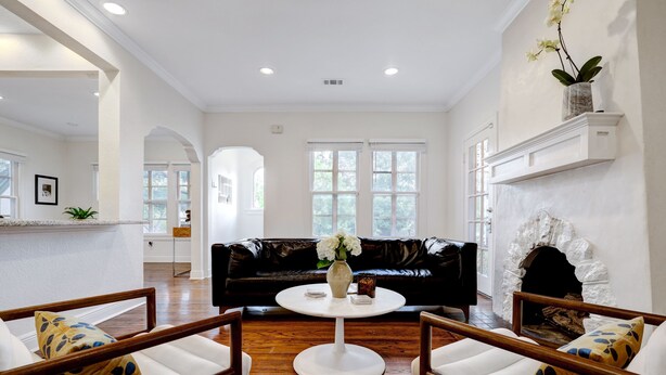A spacious living room with a black leather sofa, white armchairs, a round coffee table, and a fireplace.
