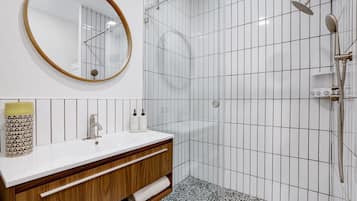 A modern bathroom with a white tiled shower, a wooden vanity with a mirror, and a white sink.