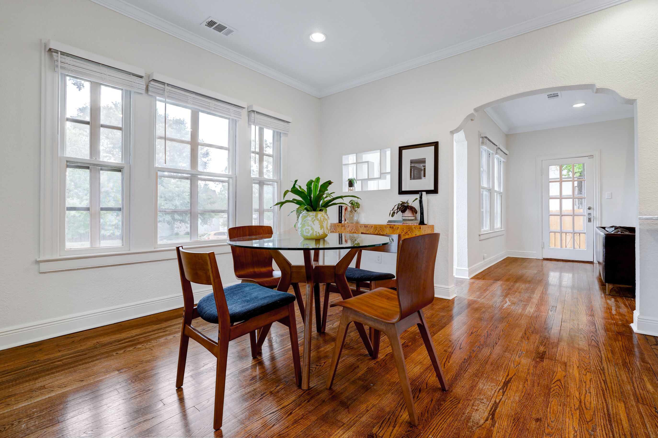A dining area with a round glass table, wooden chairs, and a potted plant.