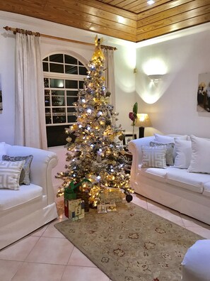 Uma sala de estar acolhedora com uma árvore de Natal decorada, sofás brancos e um tapete estampado.