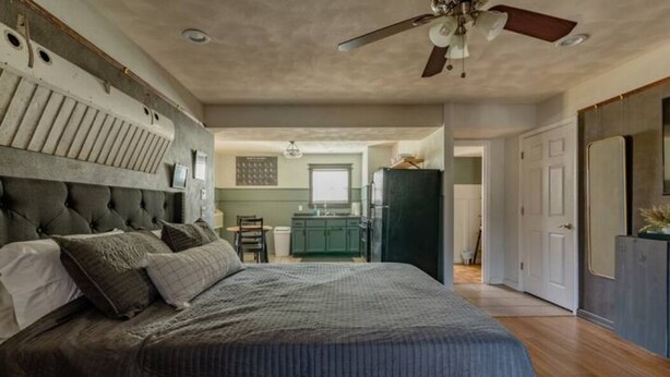 Une chambre avec un grand lit, un ventilateur de plafond et une vue sur la cuisine adjacente.
