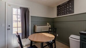 Une petite cuisine avec une table ronde en bois, une chaise, un climatiseur fixé au mur et une porte avec un rideau.