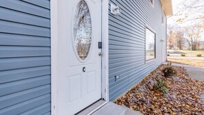 Une maison avec une porte d’entrée blanche, une fenêtre ronde et un petit jardin parsemé de feuilles d’automne.