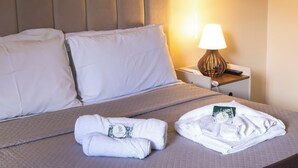 A neatly made bed with white linens, a bedside lamp, and two towels on the bed.