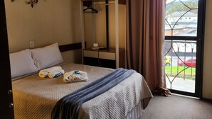 A hotel room with a bed, a ceiling fan, a window with curtains, a coat rack, and a view of the outside.