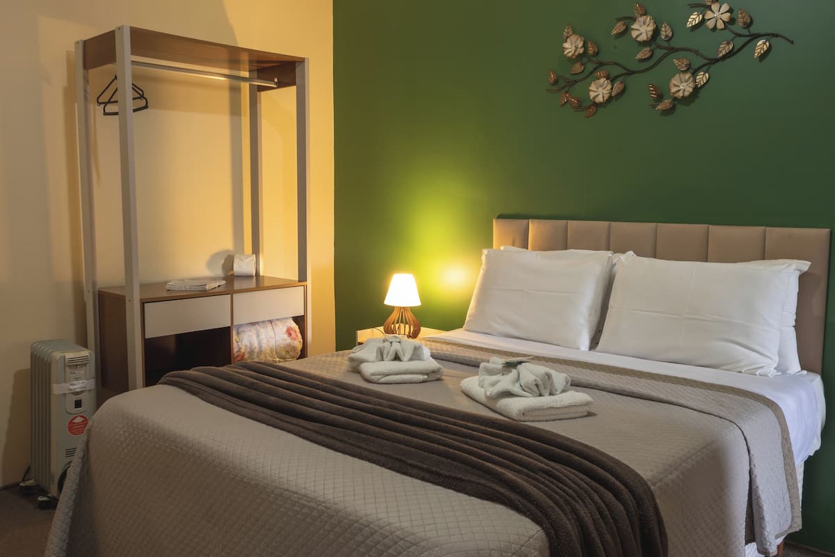 Une chambre d’hôtel comprenant un lit, une table de chevet, une lampe, un radiateur et un élément décoratif mural.