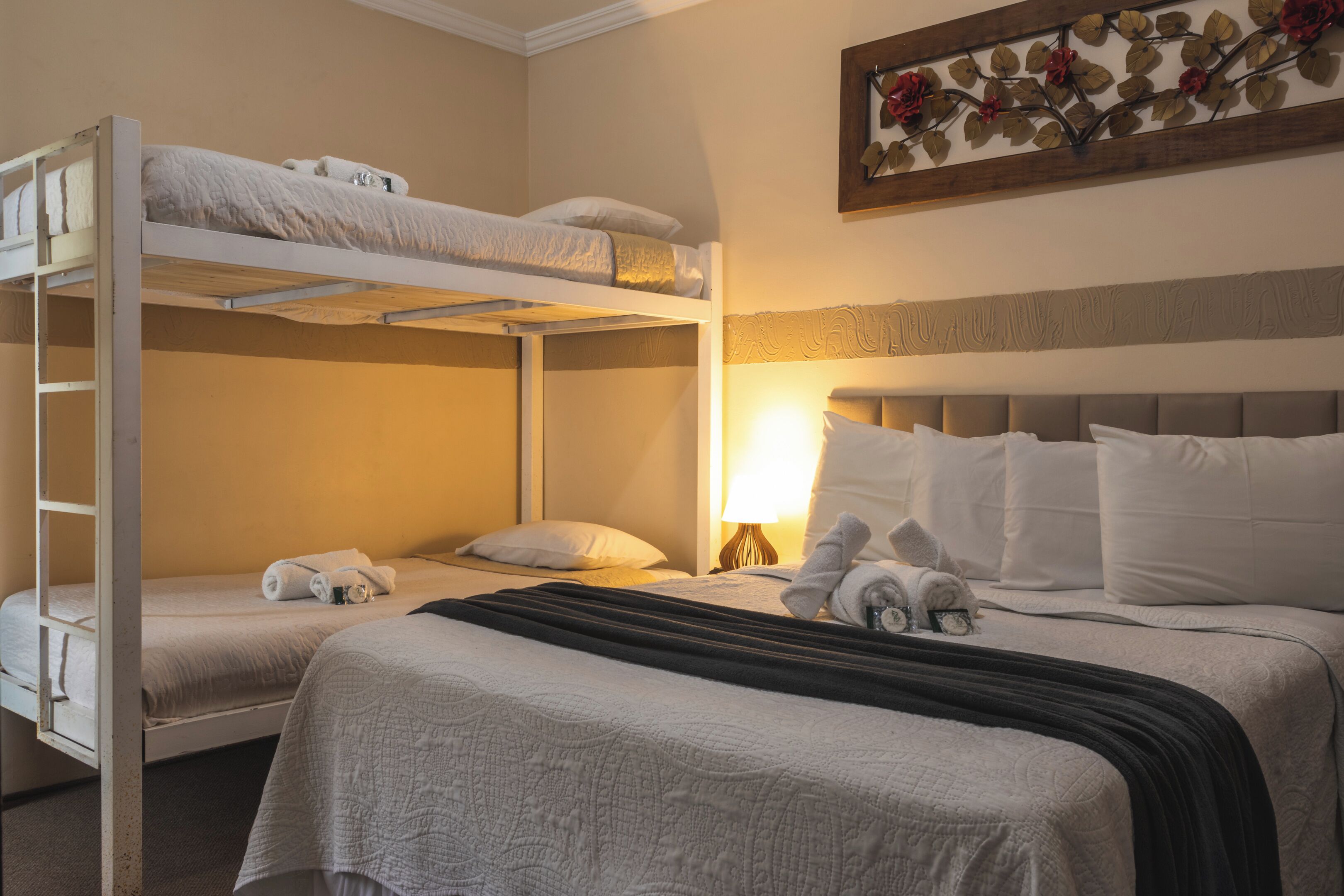 A hotel room with a bunk bed, a single bed, and a decorative wall piece.