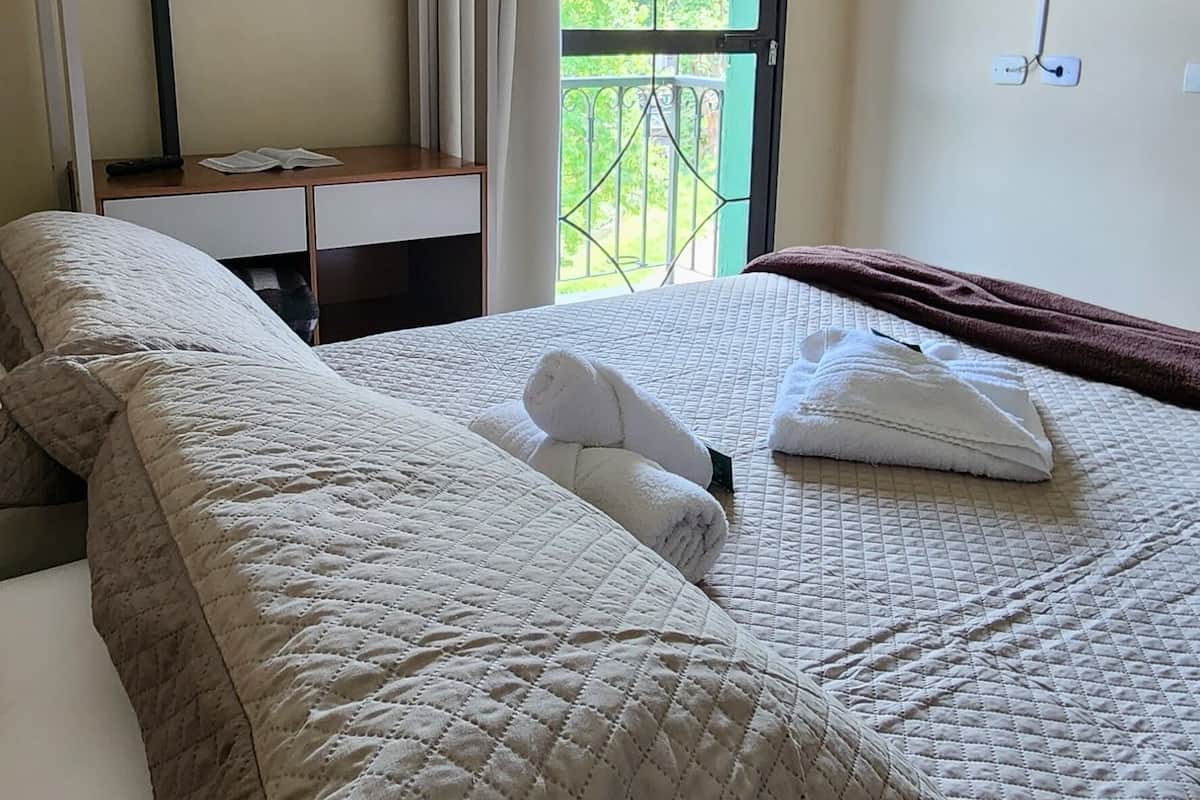 Ein Hotelzimmer mit Bett, einem Vorhangfenster, einem an der Wand montierten Fernseher und einem Balkon mit Geländer.
