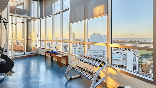 Une salle de sport moderne, dotée de grandes fenêtres, d’un appareil d’aviron et d’un banc de musculation.