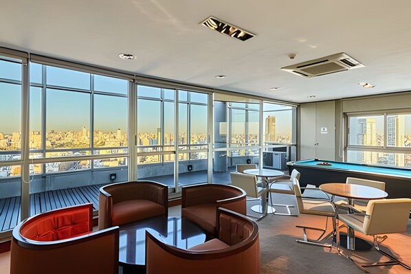 Un salon moderne doté d’une table de billard, de sièges confortables et de grandes fenêtres offrant une vue sur la ville.