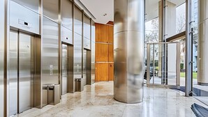 Un espace moderne avec des ascenseurs en acier inoxydable, un sol en marbre et une porte en bois en arrière-plan.