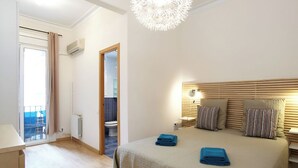 A bedroom with a large bed, a bedside table, a nightstand, a hanging light fixture, and a view of the bathroom through an open door. - Apartment Valencia - Two Bedroom Apartment (Barcelona)