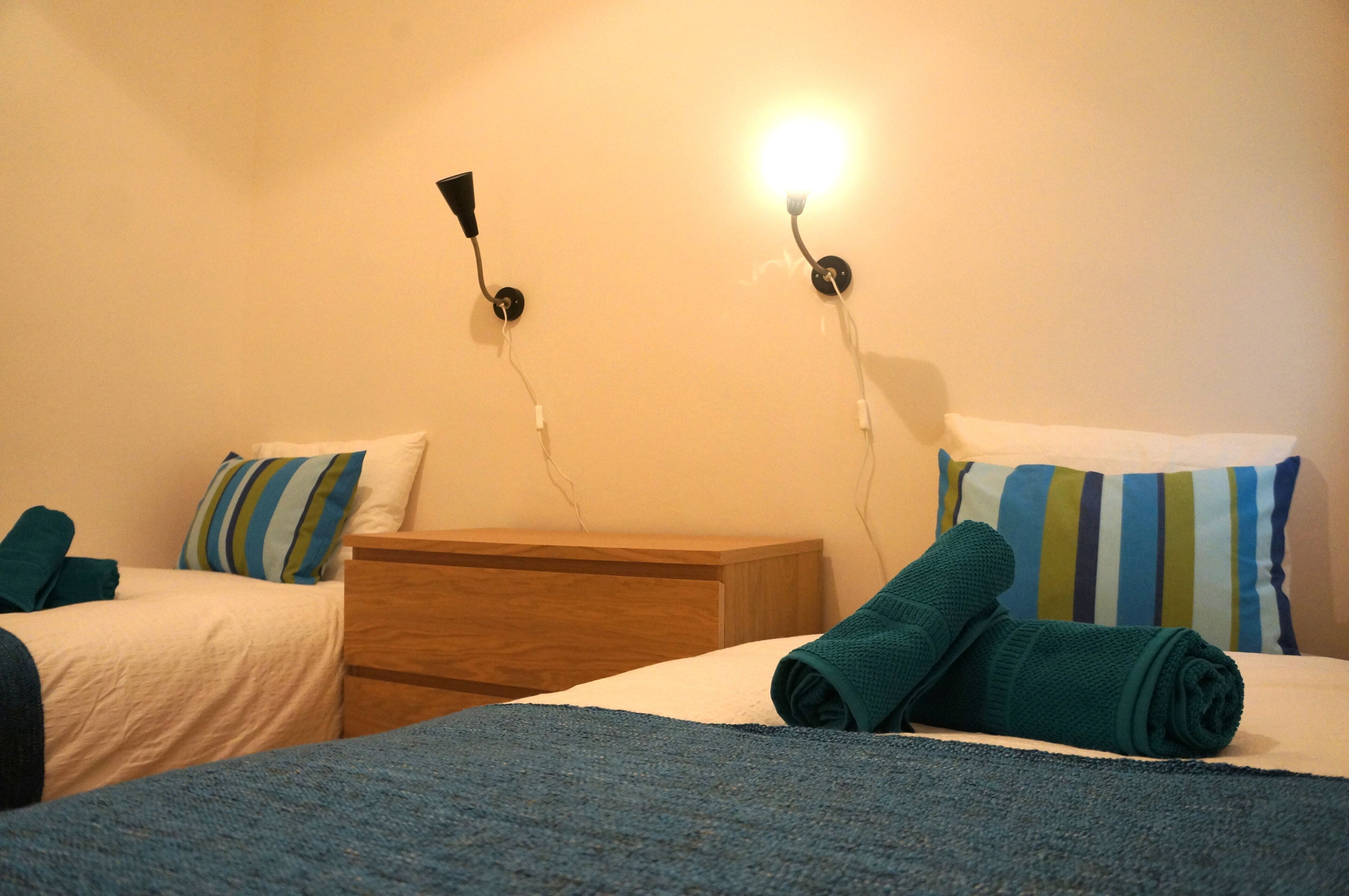 Une chambre d’hôtel avec deux lits, une table de chevet en bois et deux lampes fixées au mur.