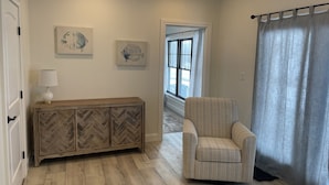 Une pièce comprenant un meuble console en bois à motifs en chevrons, un fauteuil à rayures et deux tableaux représentant des poissons, accrochés au mur.
