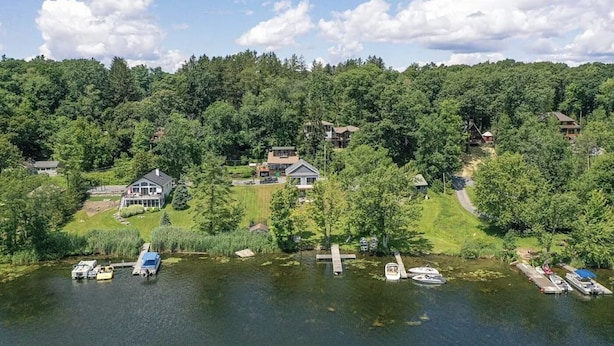 Une propriété au bord du lac comprenant plusieurs maisons, des bateaux amarrés sur la rive et une forêt en arrière-plan.