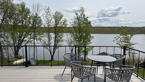 Une terrasse avec une table et des chaises, donnant sur un lac bordé d’arbres.
