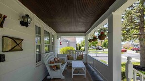 A porch with white furniture, a wooden ceiling, and hanging flower baskets.